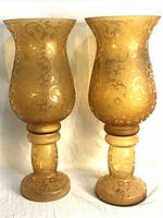 Pair of tall etched glass candle holders with golden frosted finish and intricate swirling floral etched design, shown side by side.