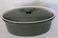 Top and side view of dark moss green ceramic casserole dish with lid showing glossy finish and oval shape
