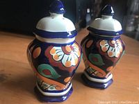Two matching ceramic salt and pepper shakers with bright Mexican folk art style decoration in navy blue, orange, green, and white colors.