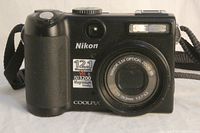 Front view of Nikon CoolPix P5100 camera, showing brand, megapixel and ISO markings, lens, and built-in flash