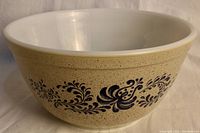 Side view of tan speckled Pyrex bowl with blue floral stencil design