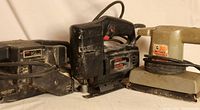 Three power tools side by side: Skil Classic belt sander, Craftsman sabre saw, and Black & Decker finishing sander.