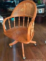 Front view of solid oak office chair showing cane back, curved armrest, and polished wood seat on caster base.