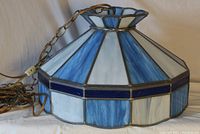 Side angle of stained glass lamp showing navy, light blue, and white panels with attached chain, cord, and toggle switch plug.