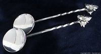 Photo showing both sterling silver spoons lying parallel, highlighting their round shallow bowls, twisted handles, and trillium flower tops.