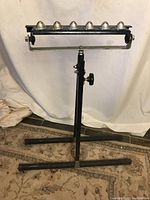 Full view of the black metal adjustable height outfeed roller stand with six ball bearing rollers and base legs.