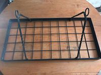 Overhead view of black wrought iron rectangular hanging pot rack showing grid surface and two hinged iron mounting arms with loops at ends