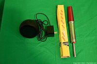 Alexa Dot with screen and power adapter cord on green background next to vintage auto antenna safety light with original yellow box
