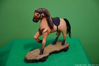 Full view of antique wooden horse pull toy on a wooden platform with four cast iron wheels, showing detailed carving and painting.