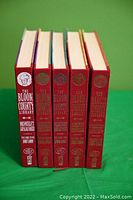 Front view of five hardcover Bloom County Library volumes showing their spines, red covers with gold and white embossed text and icons, arranged in chronological order.