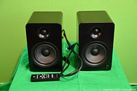 Front view showing both speakers and remote control on green background
