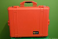 Front view of the large orange Pelican 1600 case showing sturdy plastic shell and handle on green background.