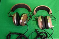 Photo showing two wired Koss studio headphones side by side on a green background, illustrating their full structure including headbands, ear pads, and coiled cords.