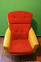 Front view showing red fabric cushions with button tufting and yellow vinyl armrest/frame against green wall and wood flooring.
