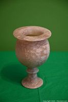Side view of the vintage hand-carved stone goblet showing the rounded bowl, flared rim, and pedestal base against a green background.