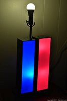 Photo showing lamp illuminated with one panel glowing blue and the other red, bulb lit, showing multi-light function and color effect.