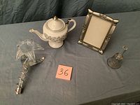 Photo of flower china tea pot, decorative glass flower, picture frame, and glass bell on display table.