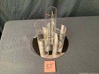 Three clear glass containers on a round mirror base from an angled top view