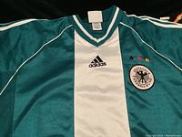 Close-up of green Adidas Germany soccer jersey front with Deutscher Fussball-Bund crest with three stars and Adidas logo