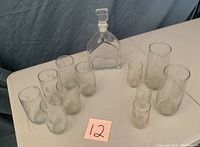Overall lot showing whiskey decanter and assortment of 11 glasses with floral etching set on white table.