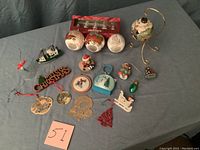 Assortment of assorted Christmas ornaments laid out including various figurines, a Christmas tree ornament, a green glass ornament, and a gold metal stand.