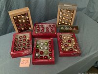 Seven boxed collections of glass Christmas ornaments arranged on dark blue fabric background.