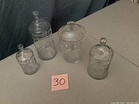 Four clear crystal candy jars displayed on a table with a pink post-it note numbered 30.