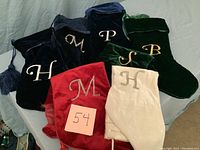 Seven velvet Christmas stockings displayed together showing varying colors and embroidered initials.