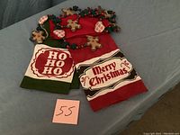 Two Christmas-themed kitchen towels and a gingerbread garland laid out on a surface with a visible lot number 55