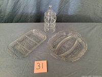 View of three crystal items on a gray cloth: tall 3-tier candy dish with lid, rectangular 3-slot relish tray, and oval 3-slot relish tray with handles, all etched floral patterns.