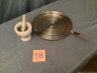 Photo showing the white marble mortar and pestle alongside a round metal splatter guard with a handle on a blue cloth background.