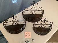 Front view of all three decorative black metal wall shelves laid out on white table with screws and anchors included.