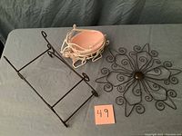 Three metal decor items on a gray cloth: a rectangular wire sleigh frame, an Easter egg wire basket holding a pink ceramic bowl, and a decorative wire wall flower.