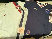 Two national soccer jerseys together showing USA white Nike jersey and navy blue Yugoslavia Adidas jersey with FSJ crest.