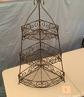 Front view of a 3 tier wire corner shelf stand with decorative scrollwork on the basket edges