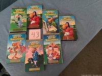 Seven VHS tapes of The Adventures of Rocky & Bullwinkle with colorful illustrated sleeves laid out on fabric surface with a note showing number 43. Sleeves show signs of wear.