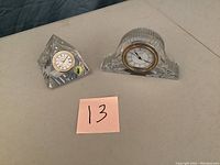 Two Waterford crystal clocks shown on a table, one pyramid shaped and one arched shaped, both crystal clear with analog clock faces.