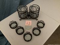 Two bottle wine holder with cylindrical glass inserts, decorative dark metal scrollwork. Five matching round wine trivets arranged in semi-circle.