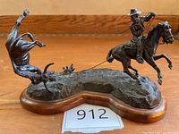 Front view of entire bronze sculpture with cowboy on horse roping bucking bull on wooden base