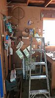 Pegboard wall with various hanging hardware items, license plates and aluminum ladder in foreground