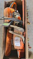 Two orange chainsaws inside a wooden box