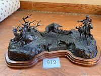 Full view of bronze sculpture on scalloped wood base showing two cowboys on horseback and central bear figure