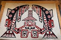 Full view of rectangular hooked rug showing ecru background, black and red stylized native art design featuring two salmon and central figure