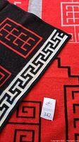 Blanket laid flat showing red field with black and white geometric storm pattern and folded edge revealing black reverse.