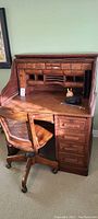 Front view of vintage roll top desk with small drawers, cubbyholes, and wooden chair in front
