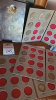 Overview of multiple open coin album pages with red felt coin holders containing several silver dollars and albums stacked