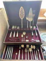 Open top view of wooden chest showing felt-lined top drawer with forks, knives and serving pieces.