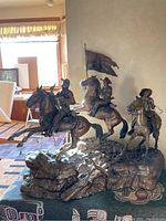 Front view of entire bronze sculpture showing three mounted cavalry figures and flowing flag on rocky base