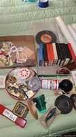 Photo of various collectible items including a vinyl 45 record, eight 8-track tapes in cases, wooden decorative items, metal bowl with assorted small metal collectibles, and cards in a box.