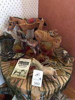 Overall lot showing the iron boots, wooden horse with colorful saddle, wooden horse on wheels, Thunderbird figure, various metal horse figurines, keychain, and a book titled 'Comanche of the Seventh.'